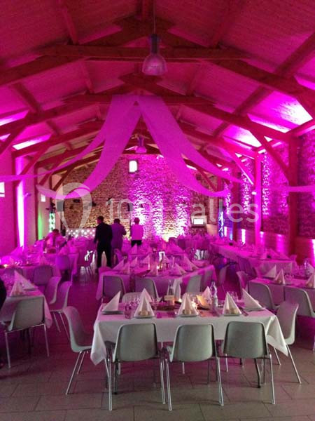 Salle de réception décorée avec des nappes blanches, éclairage rose et tables dressées pour un événement.