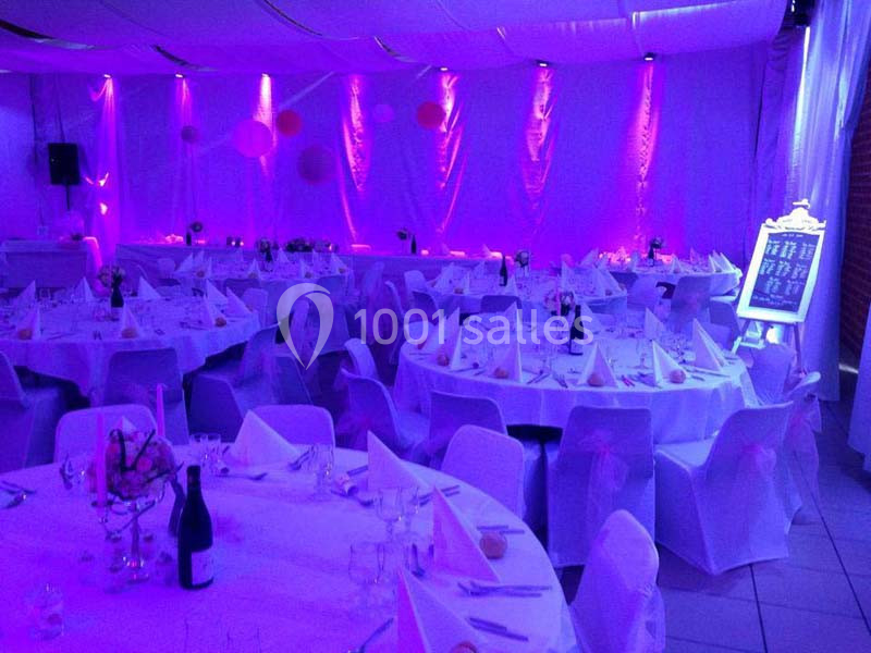 Salle de réception décorée en violet avec des tables rondes dressées de nappes blanches et serviettes pliées.