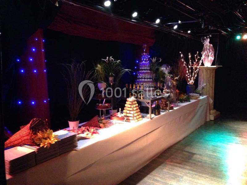 Buffet décoré avec des plats variés, une fontaine à champagne et des éléments lumineux dans une salle sombre.