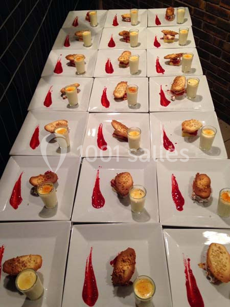 Assiettes dressées avec verrines, toasts et coulis rouge, alignées sur une table dans un cadre sombre.
