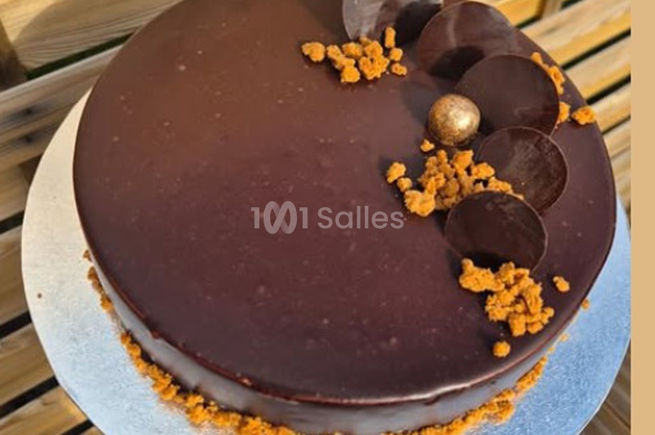 Gâteau au glaçage chocolat brillant, décoré de disques en chocolat, miettes croustillantes et une perle dorée.