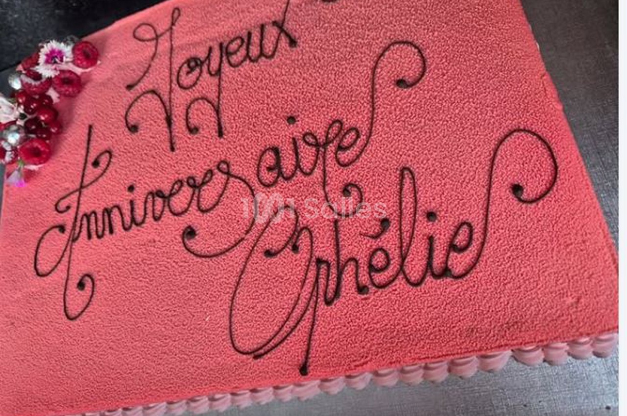 Gâteau d'anniversaire rose avec un message écrit en chocolat et des fleurs décoratives dans un coin.