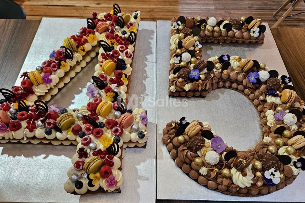 Gâteaux en forme de chiffres 4 et 5, décorés de fruits, macarons, fleurs comestibles et chocolats.