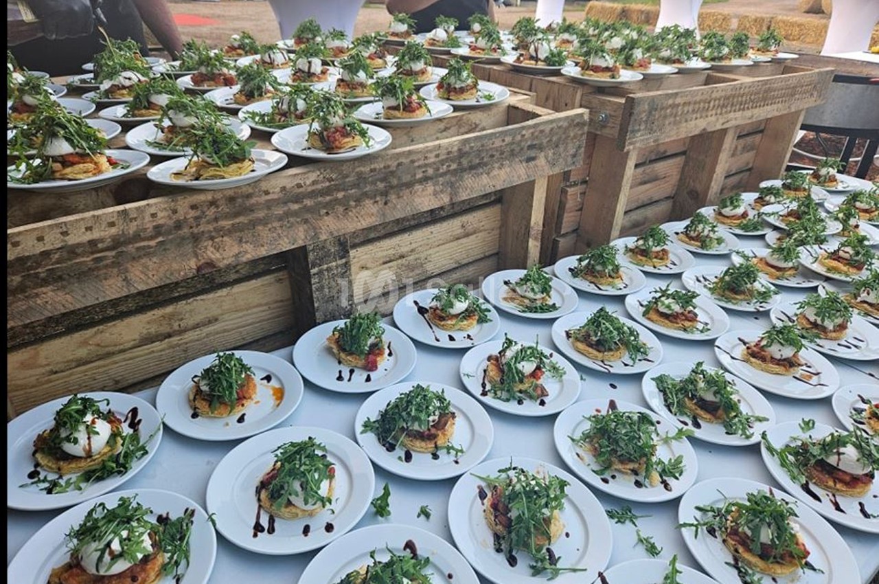 Assiettes dressées avec des entrées garnies de roquette et de sauce balsamique, disposées sur des tables en bois.