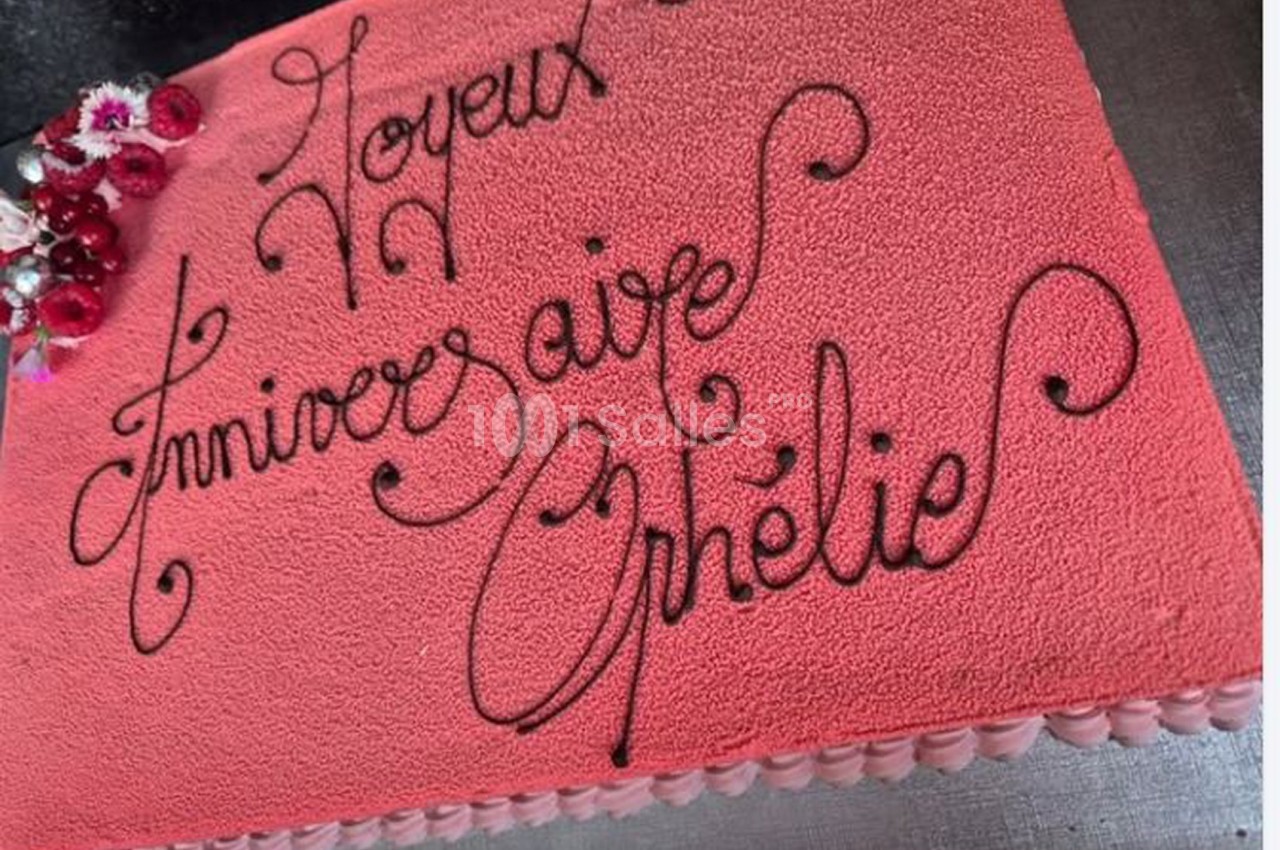 Gâteau d'anniversaire rose avec un message écrit en chocolat et des fleurs décoratives dans un coin.
