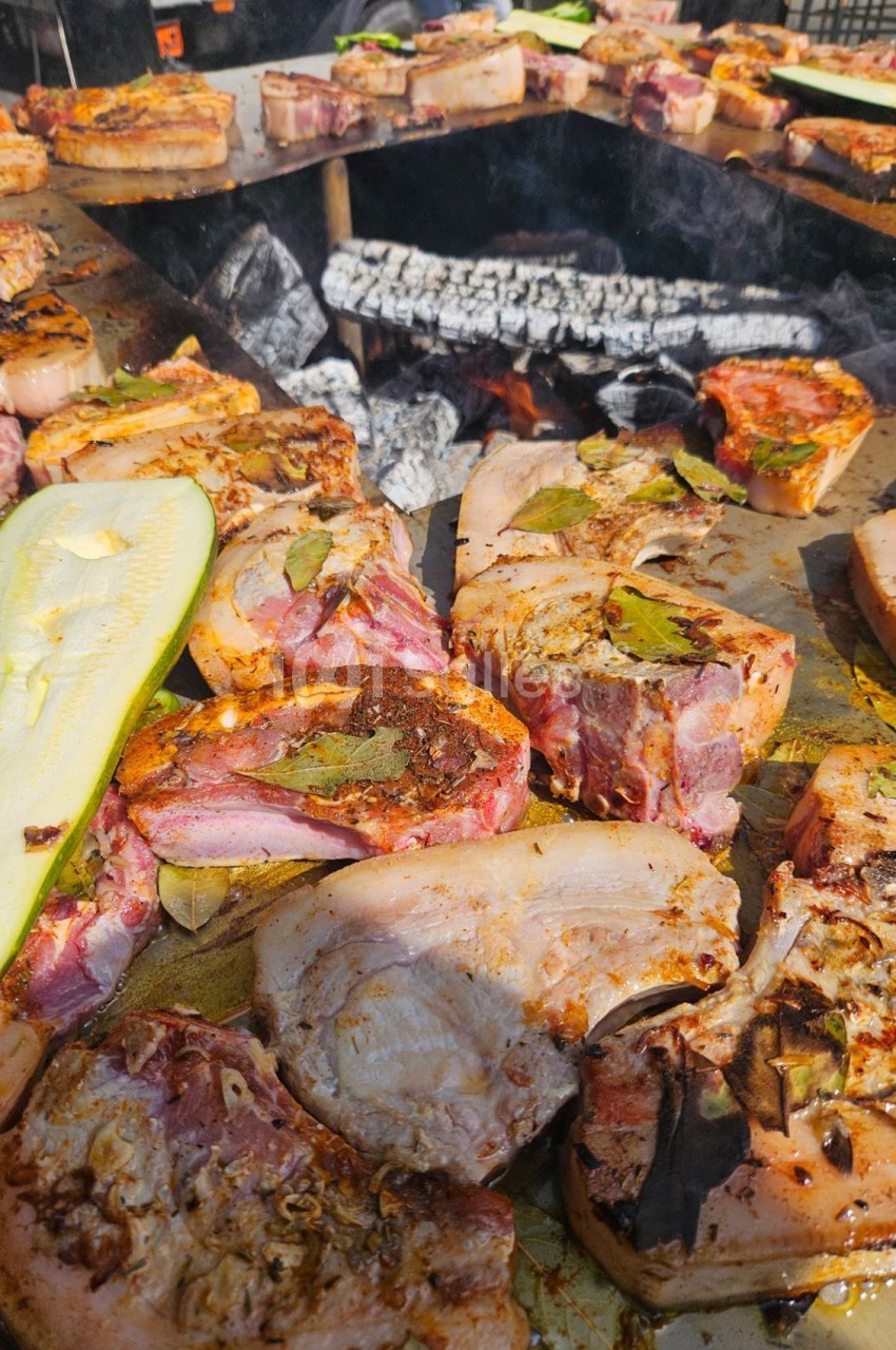 Viandes et légumes grillant sur un barbecue au feu de bois, avec des braises incandescentes en arrière-plan.