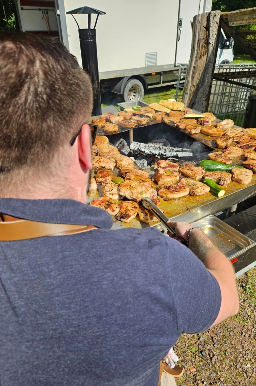 Un homme en train de griller des viandes et des légumes sur un barbecue en plein air.