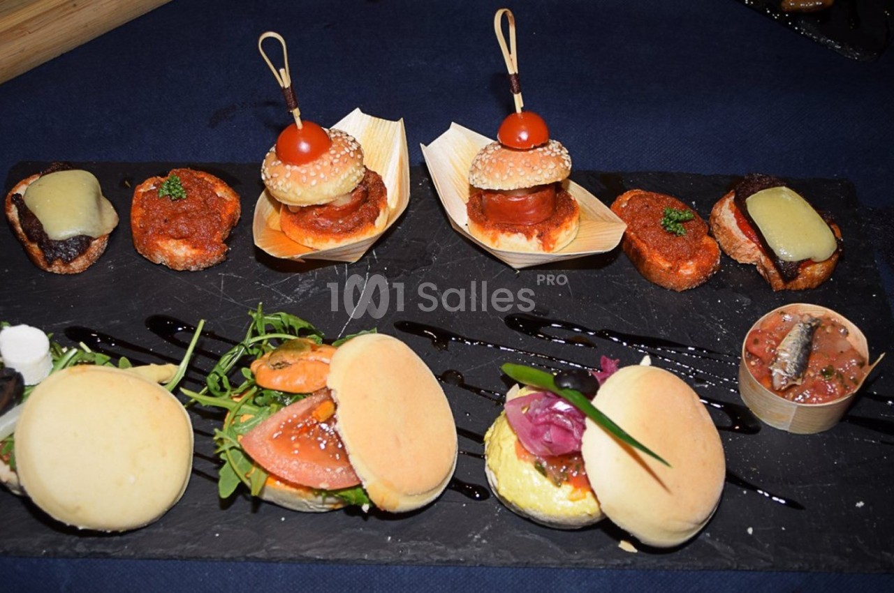 Plateau de mini-burgers, bouchées et verrine sur ardoise, décoré de sauce balsamique et herbes fraîches.