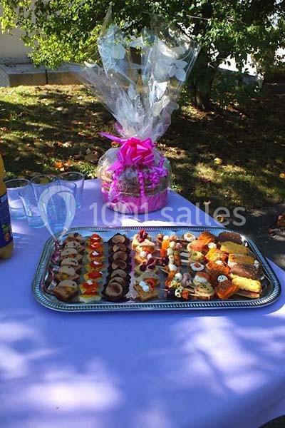 Plateau de petits fours variés sur une table violette en extérieur, avec un panier cadeau et des verres à proximité.