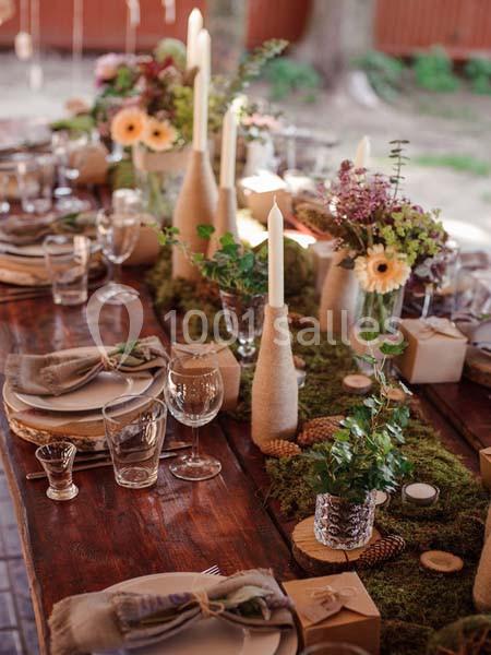 Table en bois décorée de bougies, fleurs, mousse et vaisselle, créant une ambiance rustique et élégante.