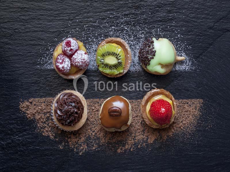 Assortiment de mini-tartelettes garnies de fruits, chocolat et crème, disposées sur une ardoise saupoudrée de cacao.