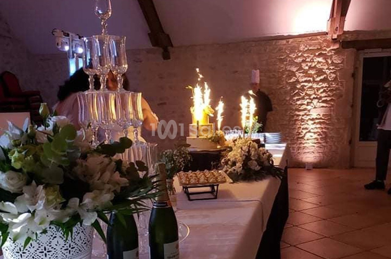 Table de réception décorée avec des fleurs, des bouteilles de champagne et un gâteau illuminé par des cierges magiques.