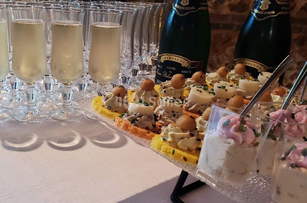 Plateau d'amuse-bouches variés avec verrines et flûtes de champagne sur une table blanche.
