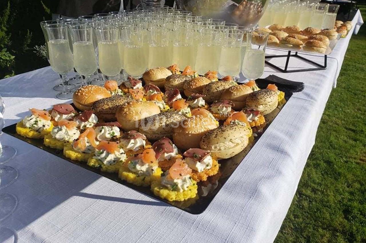 Plateau de mini-sandwichs garnis et verres de boisson claire disposés sur une table blanche en extérieur.