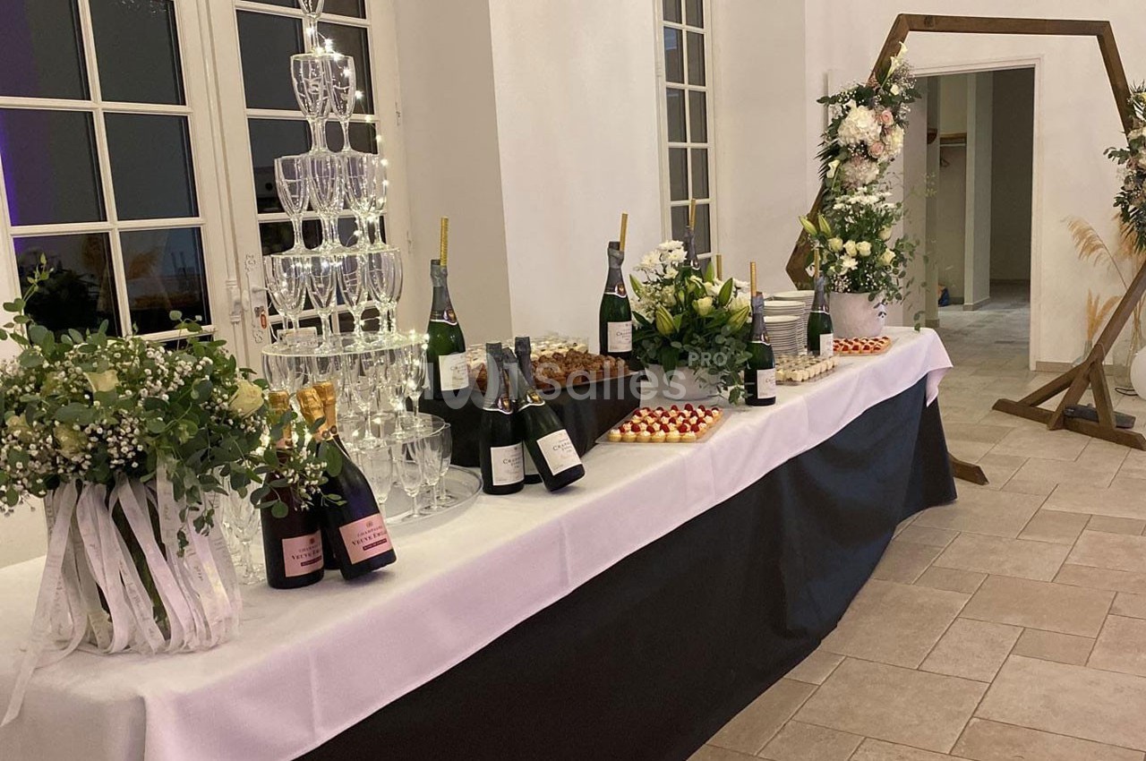 Table décorée avec des bouteilles de champagne, une pyramide de verres, des fleurs et des desserts dans une salle lumineuse.