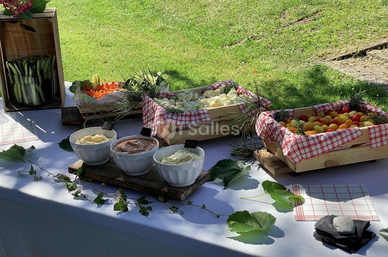 Buffet en plein air avec légumes frais, sauces en bols et décorations naturelles sur une nappe blanche.