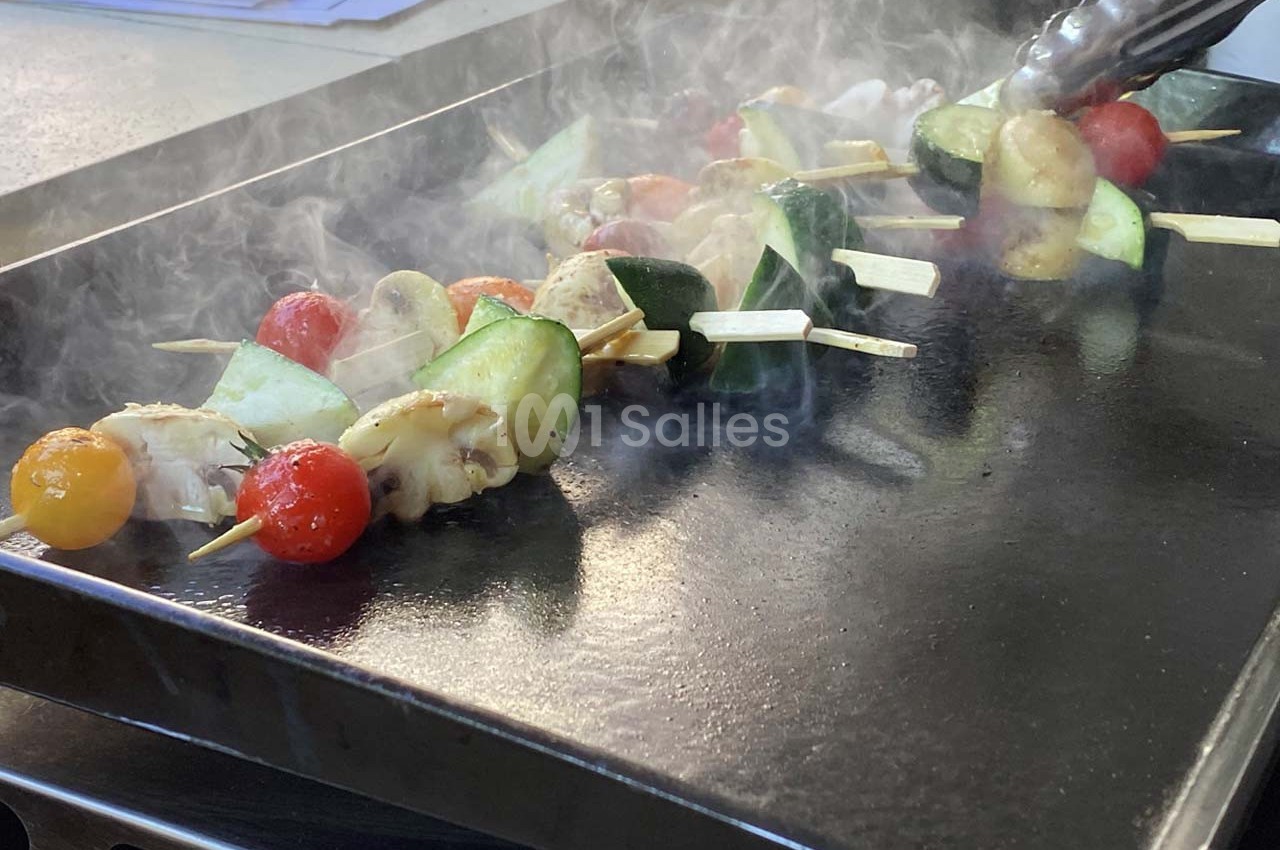 Brochettes de légumes variés grillant sur une plaque chaude, avec de la vapeur s'élevant autour.