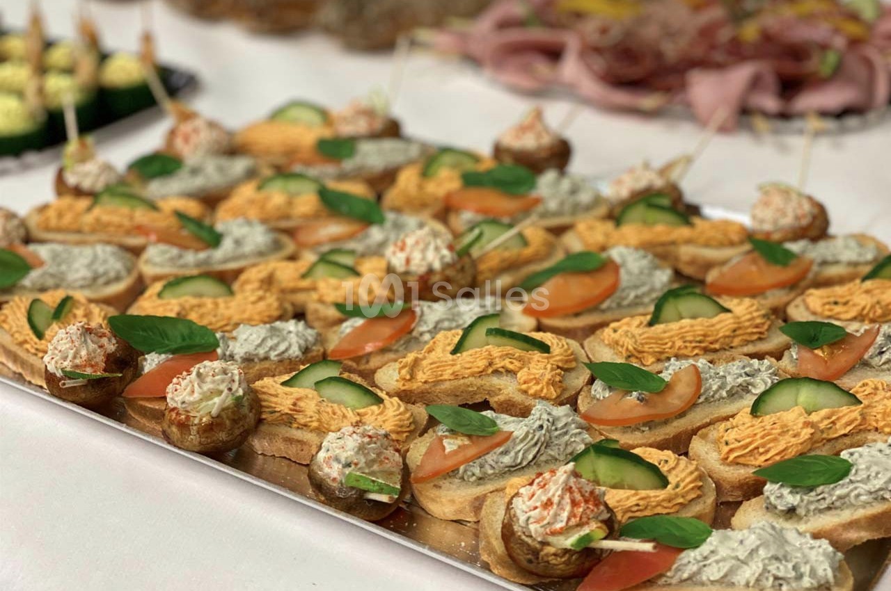 Plateau de canapés variés garnis de légumes, crème et herbes, disposés sur une table pour un buffet.