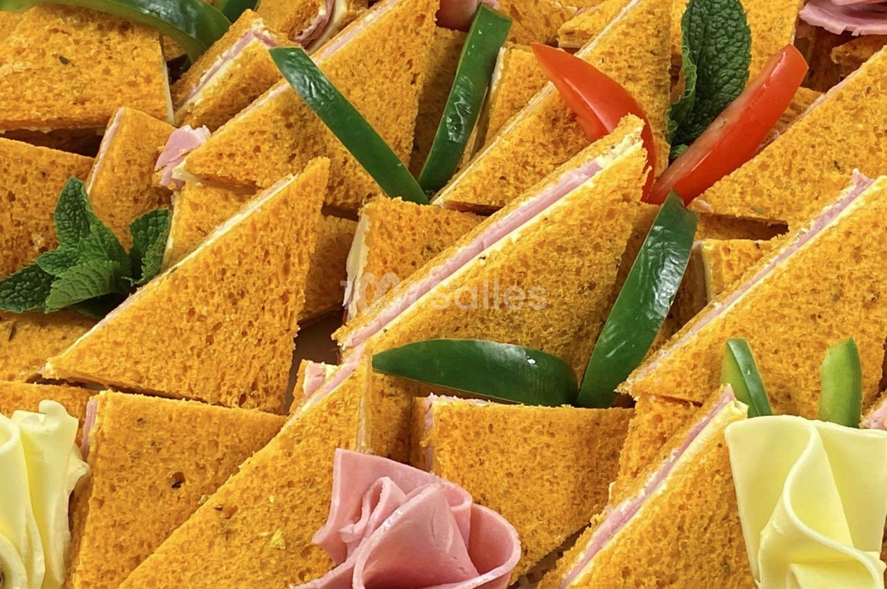 Triangles de pain orange garnis de jambon et fromage, décorés de poivrons, menthe et roulés de charcuterie.