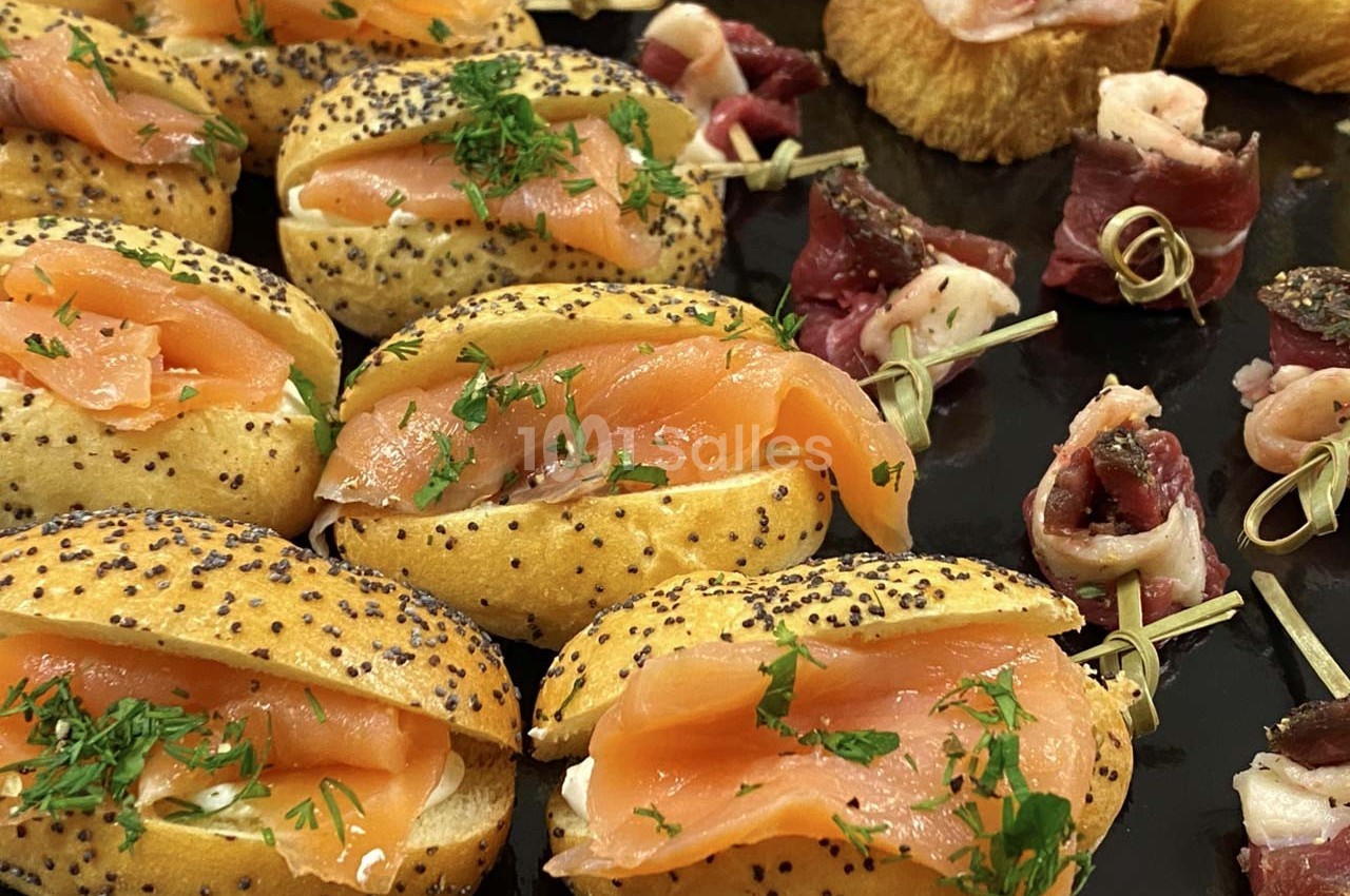 Assortiment de mini-sandwichs au saumon et d'amuse-bouches garnis de viande sur un plateau noir.