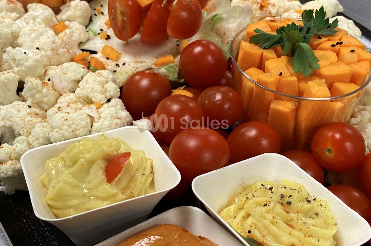 Plateau de légumes crus variés avec tomates cerises, chou-fleur, dés de carotte et sauces en accompagnement.