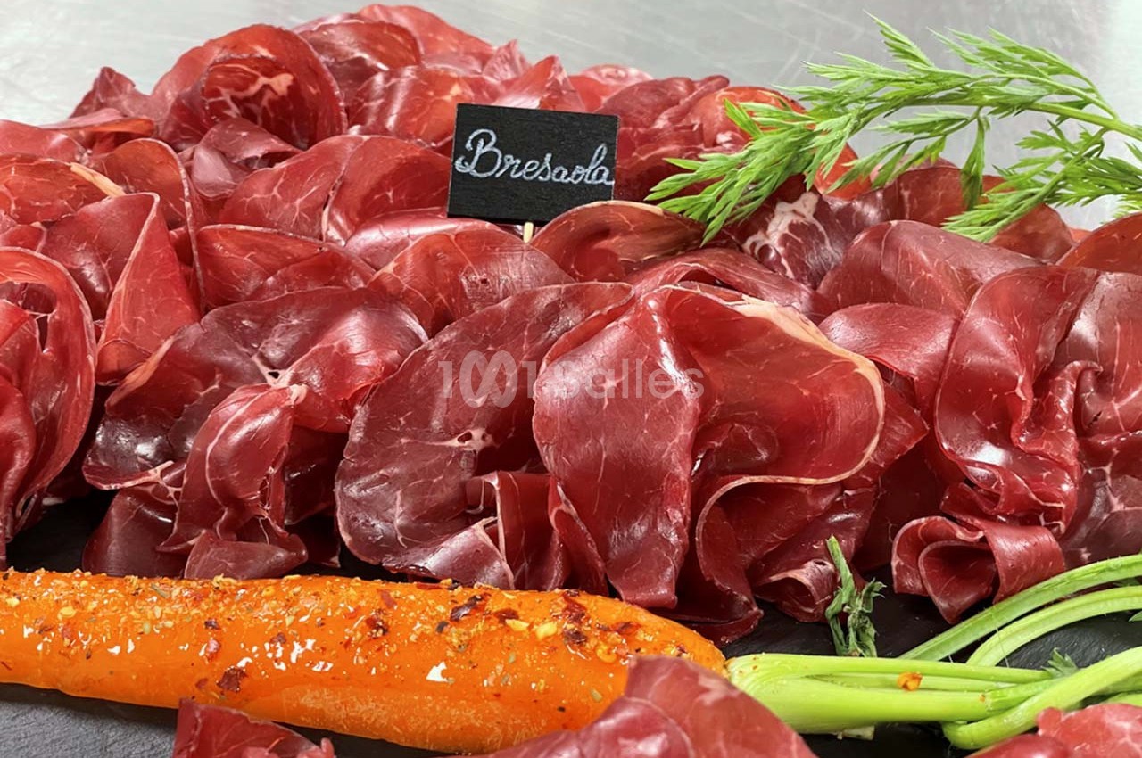 Tranches fines de bresaola disposées sur un plateau avec une carotte assaisonnée et une étiquette noire.