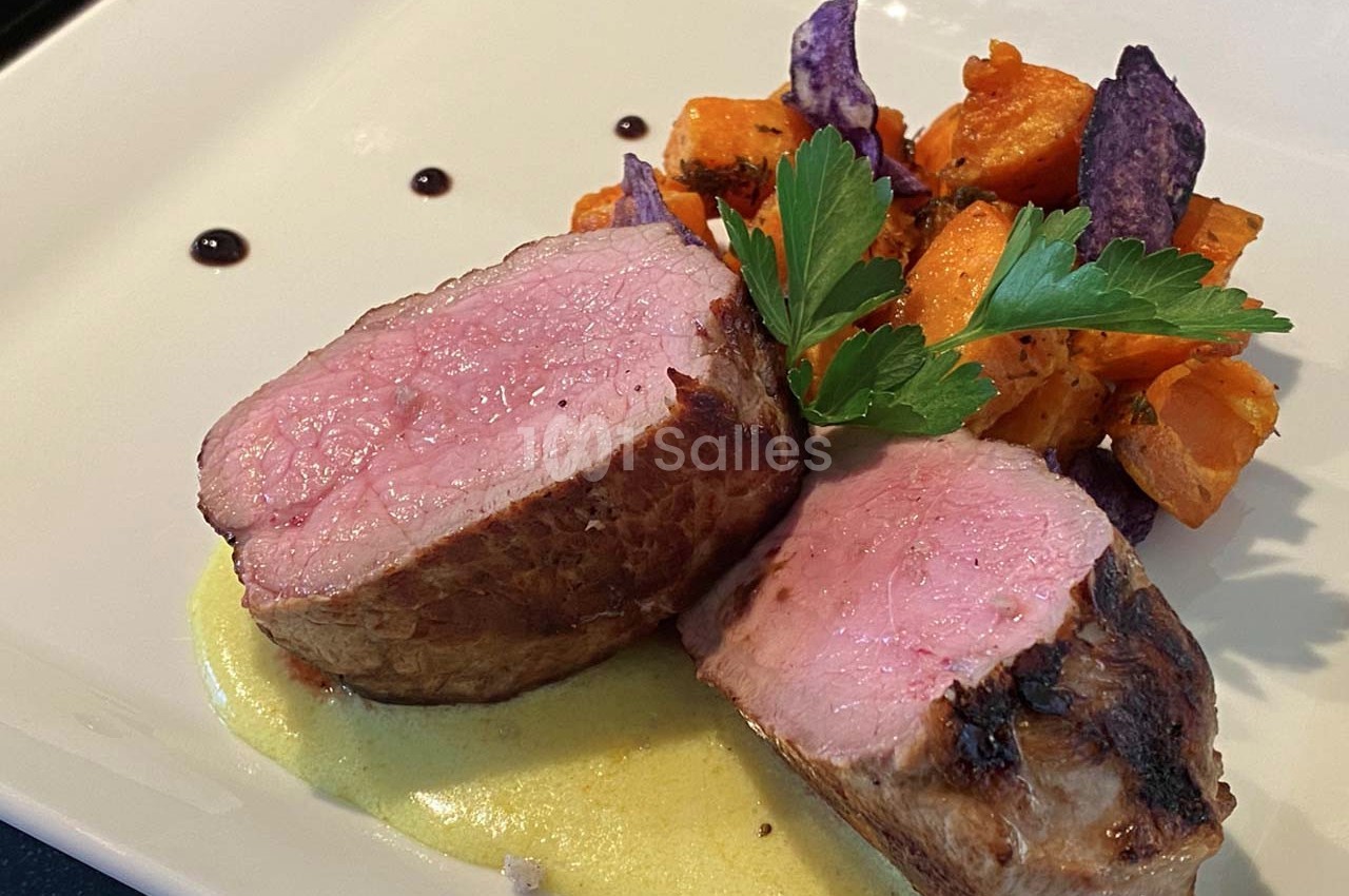 Filet de viande rosé sur sauce crémeuse, accompagné de patates douces et chips violettes, décoré de persil.