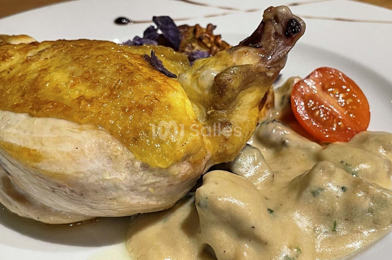 Poulet rôti avec peau dorée, accompagné de sauce crémeuse, légumes violets et demi-tomate cerise sur une assiette blanche.