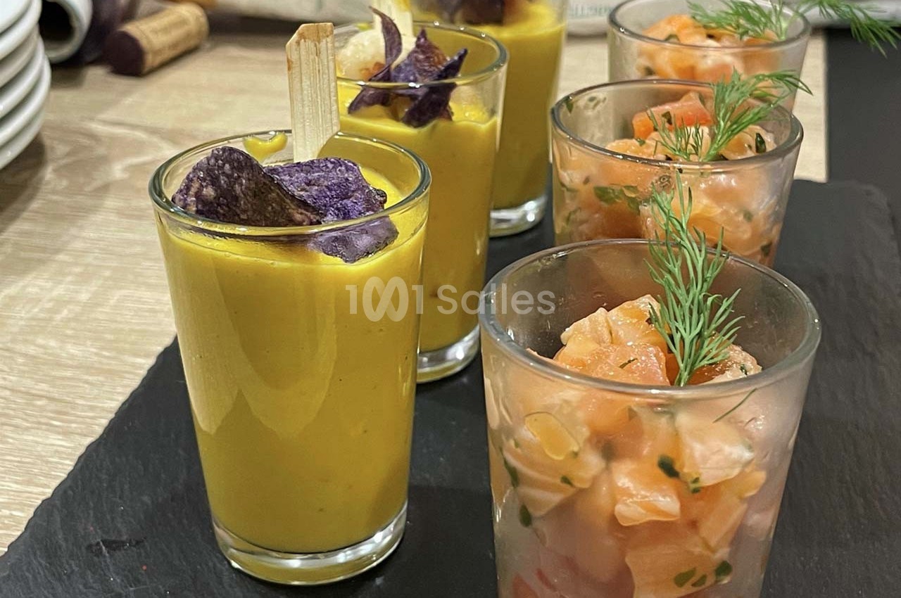 Verrines de soupe jaune garnies de chips violettes et tartares de saumon décorés d'aneth, présentées sur un plateau.