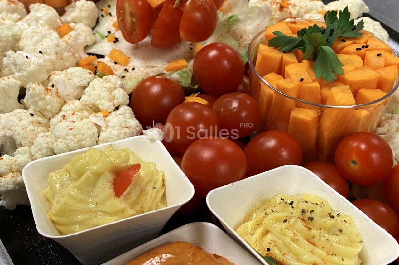 Plateau de légumes crus variés avec tomates cerises, chou-fleur, dés de carotte et sauces en accompagnement.