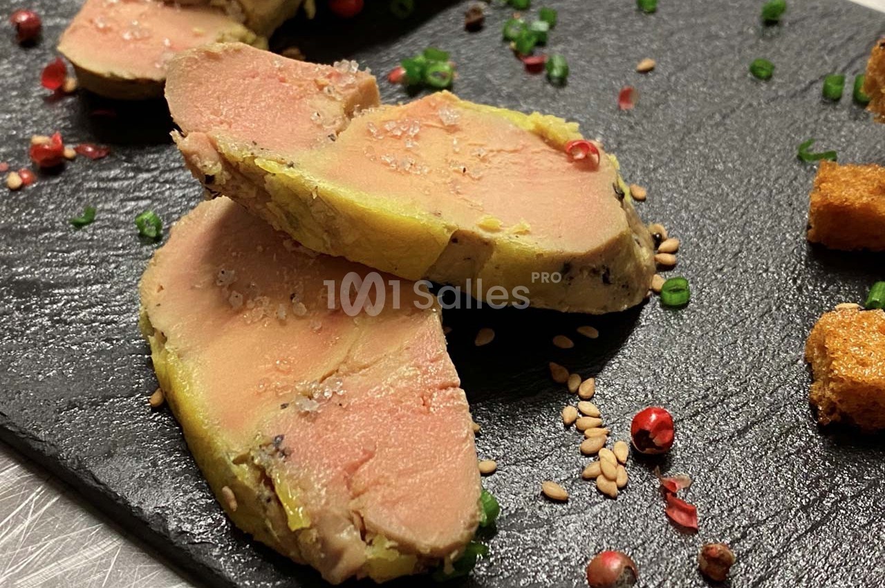 Tranches de foie gras disposées sur une ardoise avec graines, herbes et croûtons en garniture.