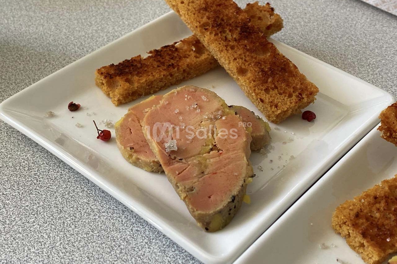 Tranches de foie gras sur une assiette blanche, accompagnées de toasts dorés et de quelques grains de sel.