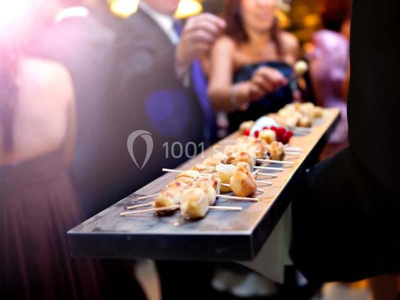 Plateau de brochettes apéritives servi lors d'un événement, avec des invités en arrière-plan flou.