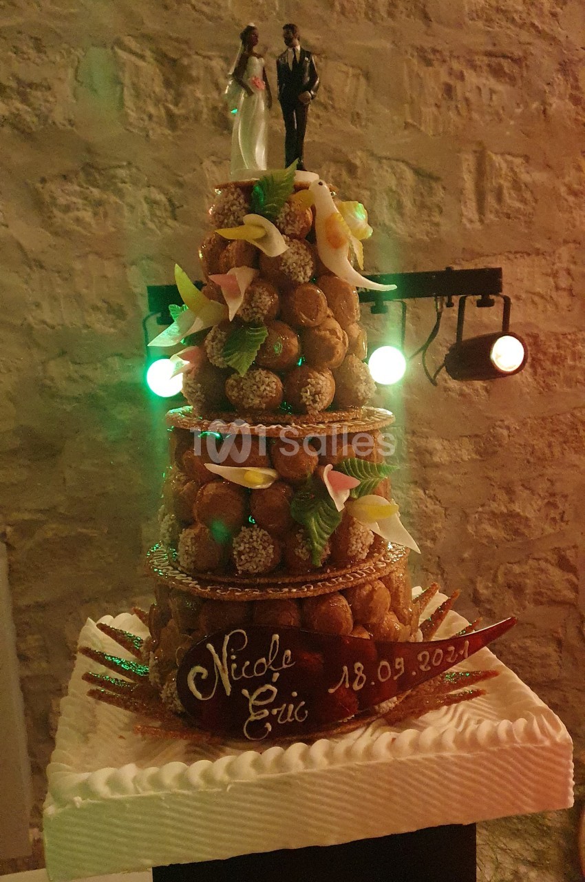 Pièce montée de choux décorée de fleurs en sucre et figurines de mariés, avec une inscription personnalisée.