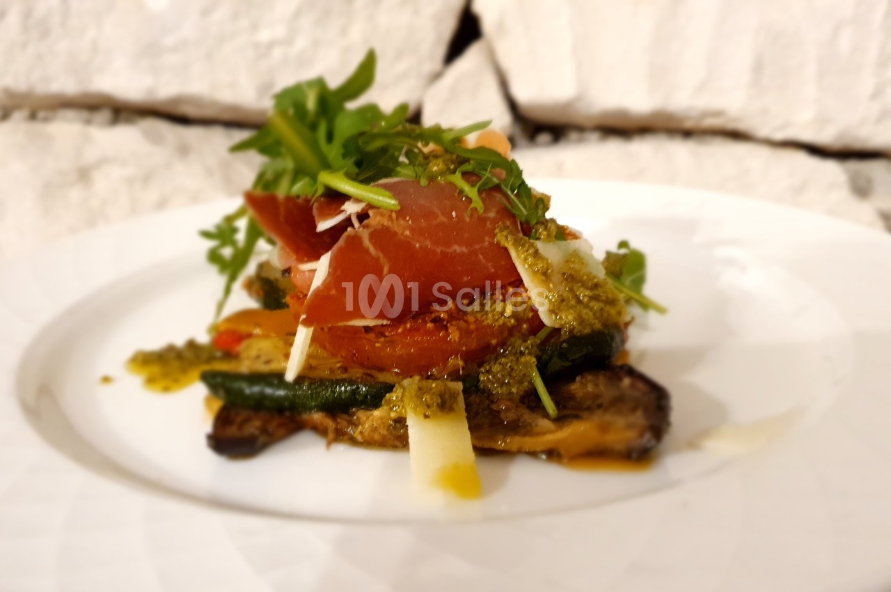 Assiette de légumes grillés garnie de jambon cru, roquette, copeaux de fromage et sauce pesto.