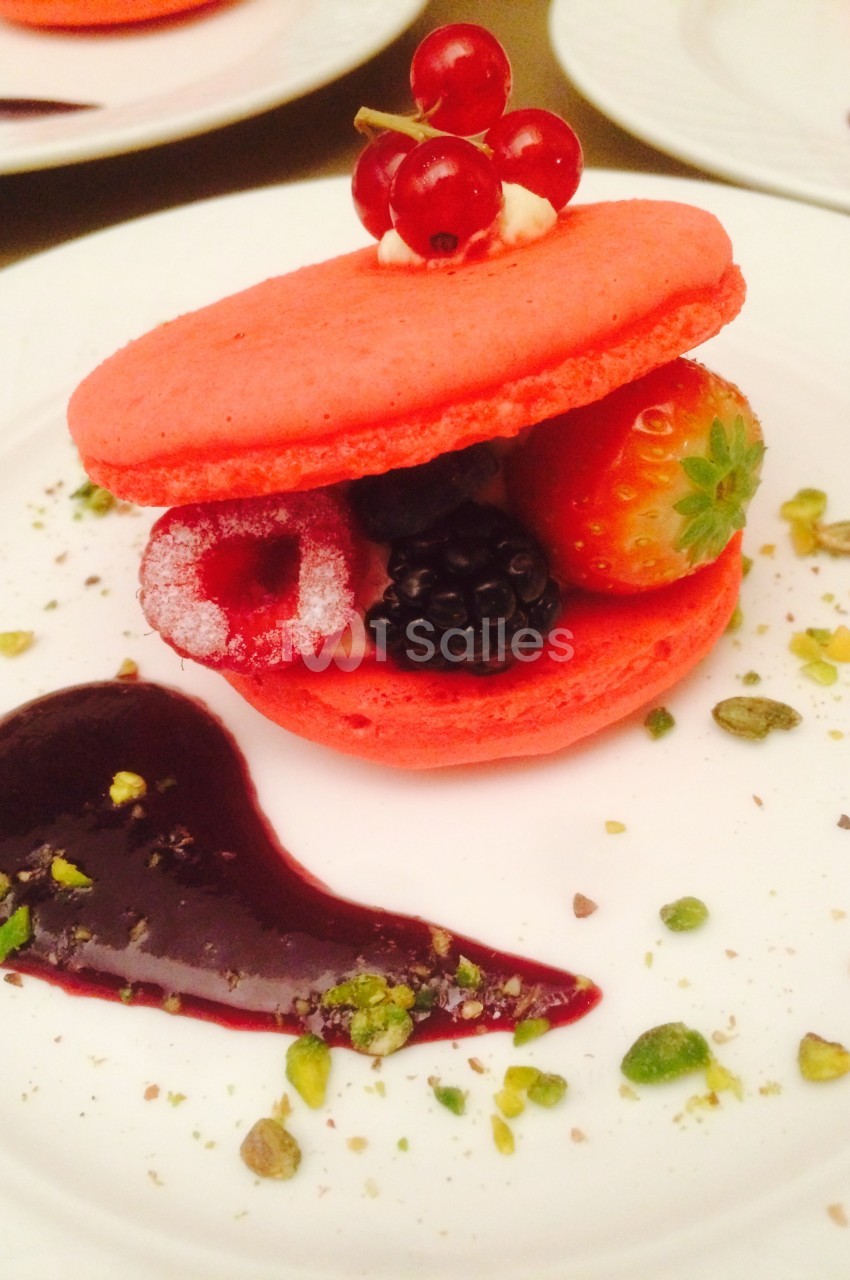 Macaron rouge garni de fruits rouges et noirs, décoré de groseilles, pistaches concassées et coulis de fruits.
