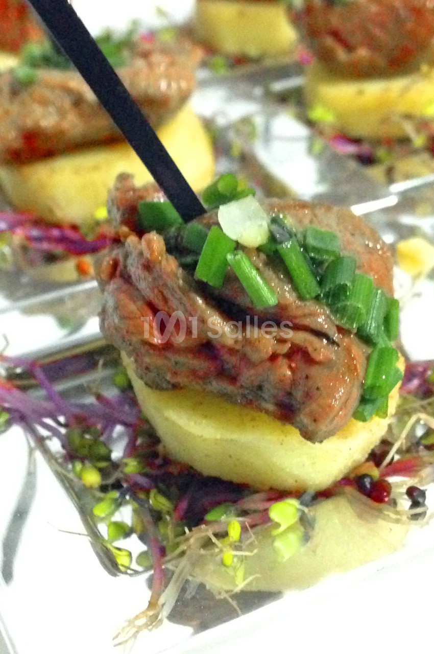 Bouchée apéritive composée de viande garnie de ciboulette sur une base de pomme de terre et jeunes pousses.
