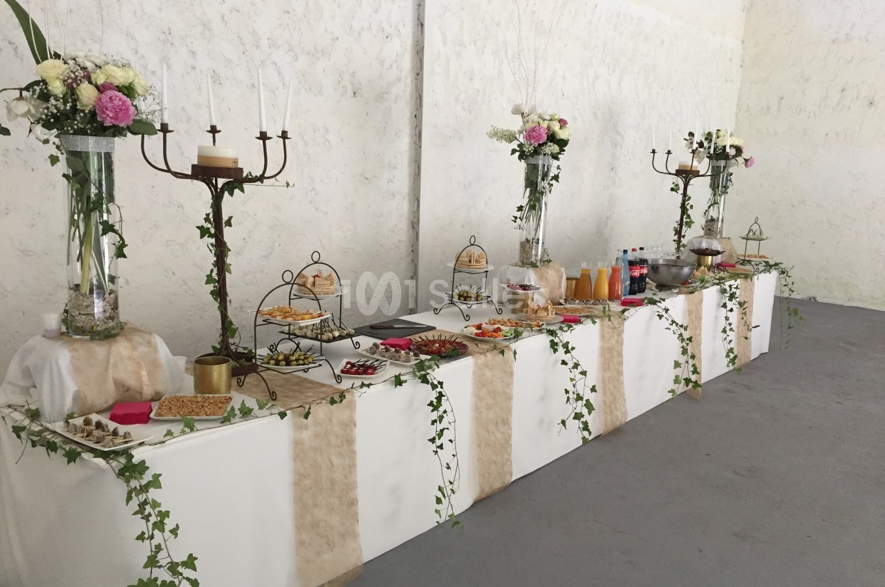Table de buffet décorée avec des fleurs, des chandeliers et des plats variés, dans une salle aux murs clairs.