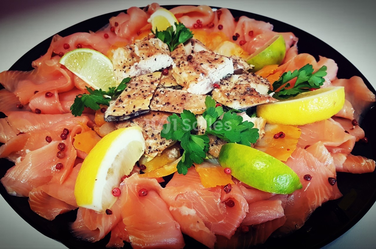 Assiette garnie de tranches de saumon fumé, morceaux de poisson grillé, rondelles de citron et herbes fraîches.
