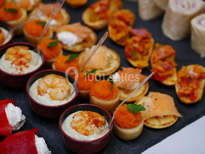 Assortiment de bouchées apéritives comprenant crevettes, saumon, légumes et roulés, disposées sur un plateau.