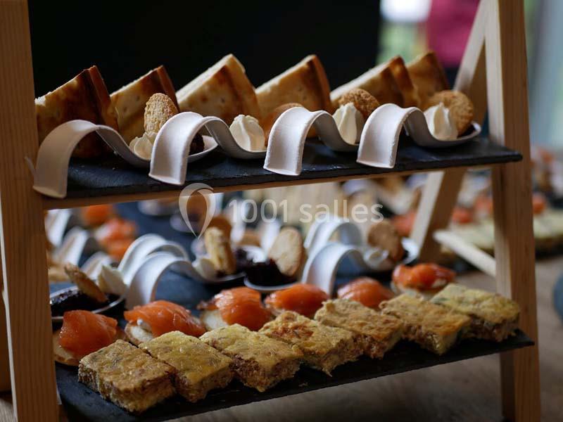 Plateau de service à deux étages avec des amuse-bouches variés, dont saumon fumé, quiches et petits pains.