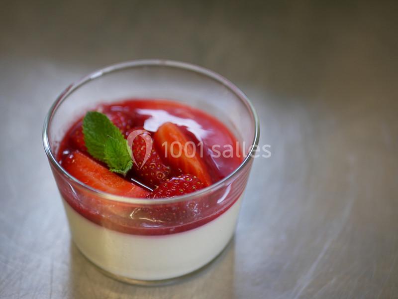 Dessert de panna cotta dans un verre, garni de coulis de fraise, morceaux de fraises fraîches et une feuille de menthe.