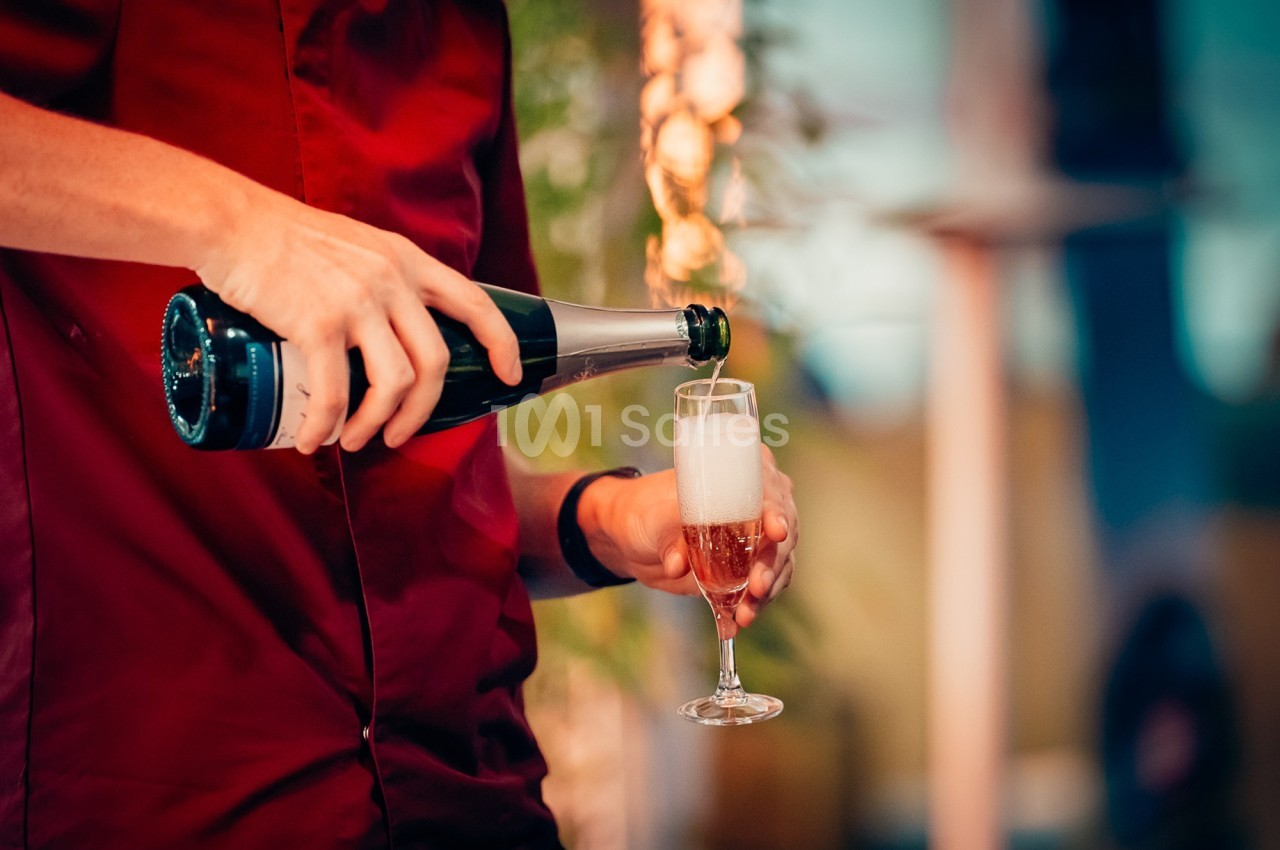 Une personne verse du champagne dans une flûte, avec un arrière-plan flou et des décorations lumineuses.