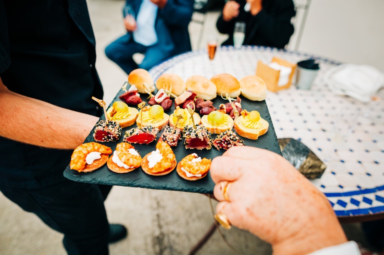 Plateau d'amuse-bouches variés avec canapés, brochettes et mini-sandwichs servi lors d'un événement en extérieur.
