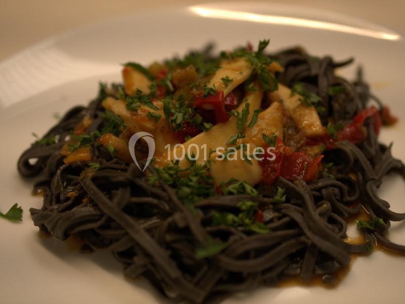 Pâtes noires servies avec des morceaux de poisson, poivrons rouges et persil sur une assiette blanche.