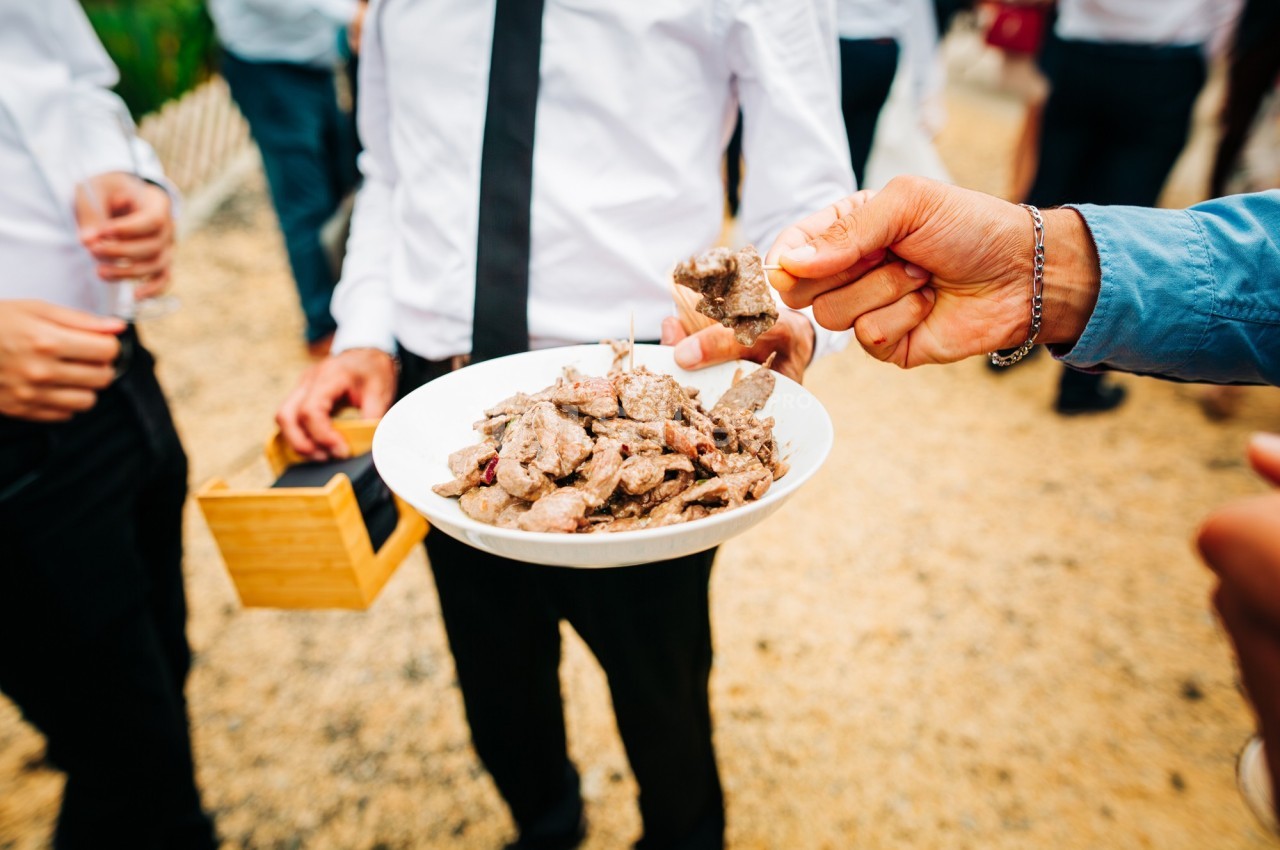 Un serveur propose un plat de morceaux de viande à des invités lors d'un événement en extérieur.