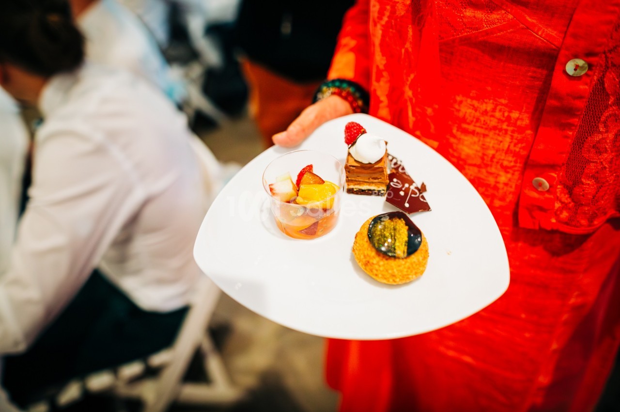Une personne tient une assiette contenant des desserts variés, dont une tartelette, un gâteau au chocolat et des fruits.