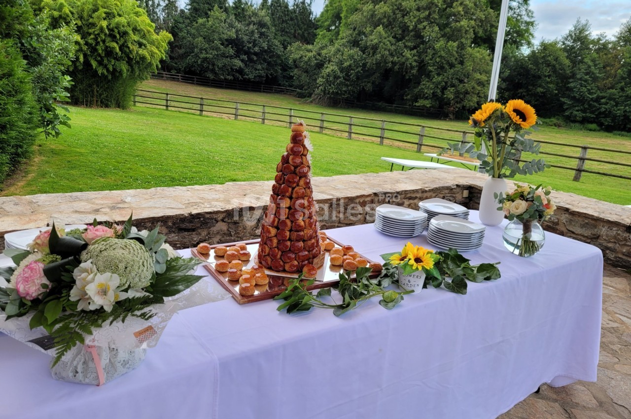 Table dressée en extérieur avec une pièce montée de choux, des bouquets de fleurs et des assiettes empilées.