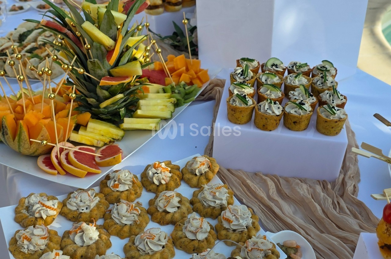 Plateau de buffet avec fruits frais, verrines garnies et petits amuse-bouches disposés sur une table blanche.