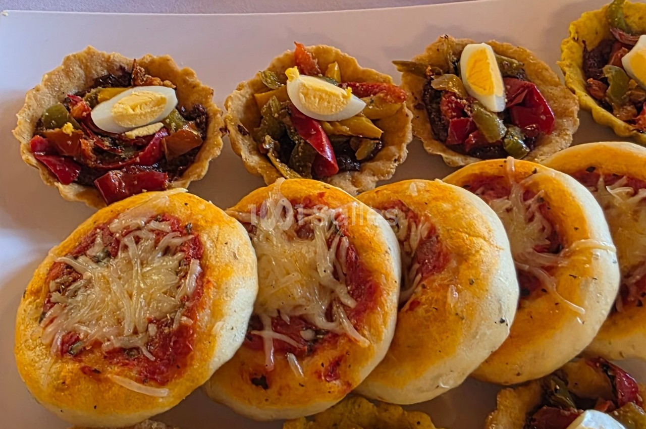 Assortiment de mini pizzas au fromage et de tartelettes garnies de légumes et œufs durs sur un plateau.